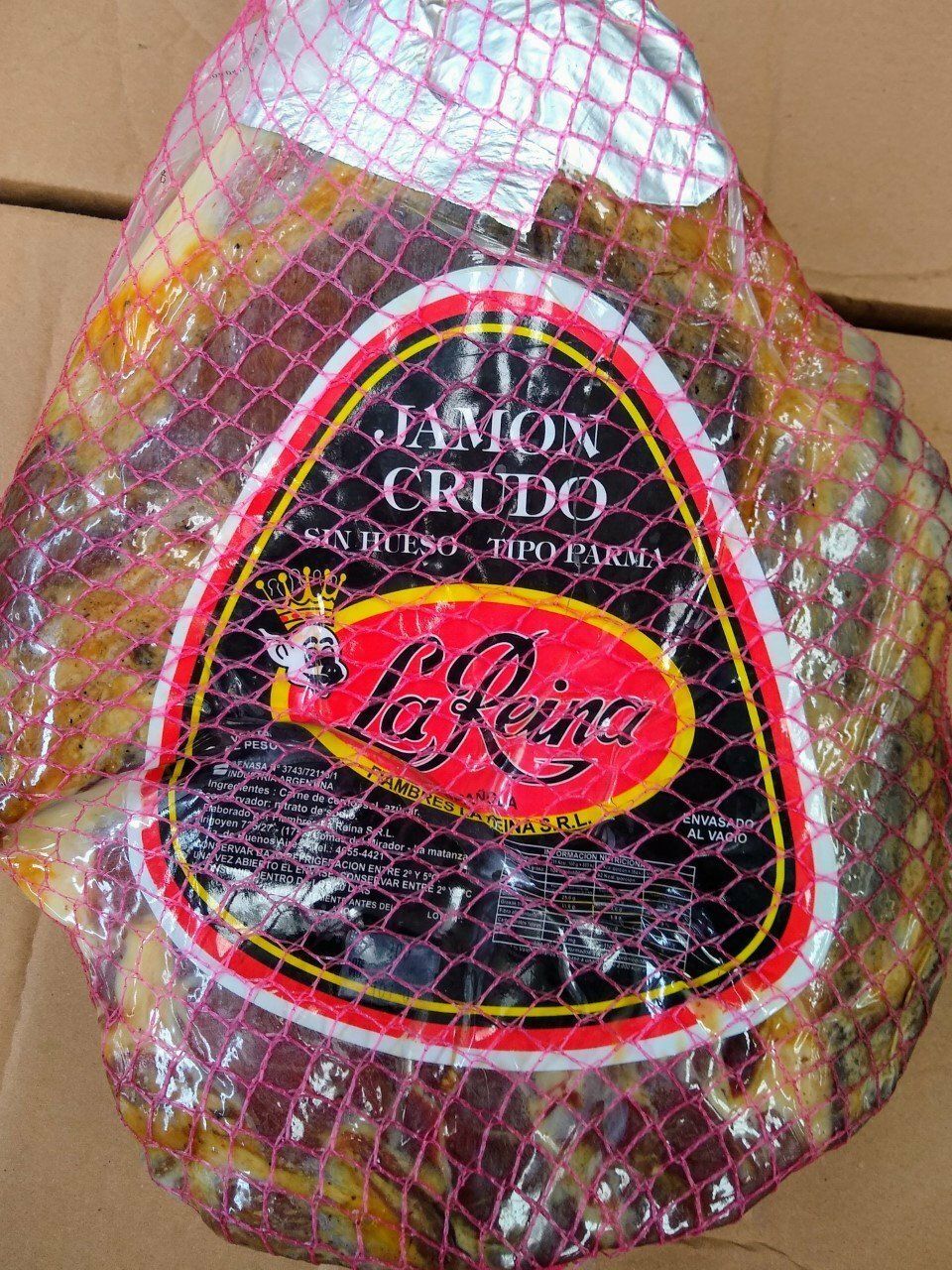 Jamón curado envuelto con una etiqueta roja y negra en una red rosa.