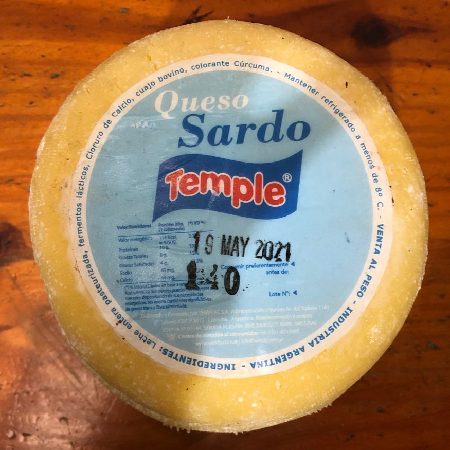 Rueda redonda de queso Queso Sardo Temple con etiqueta azul sobre superficie de madera.