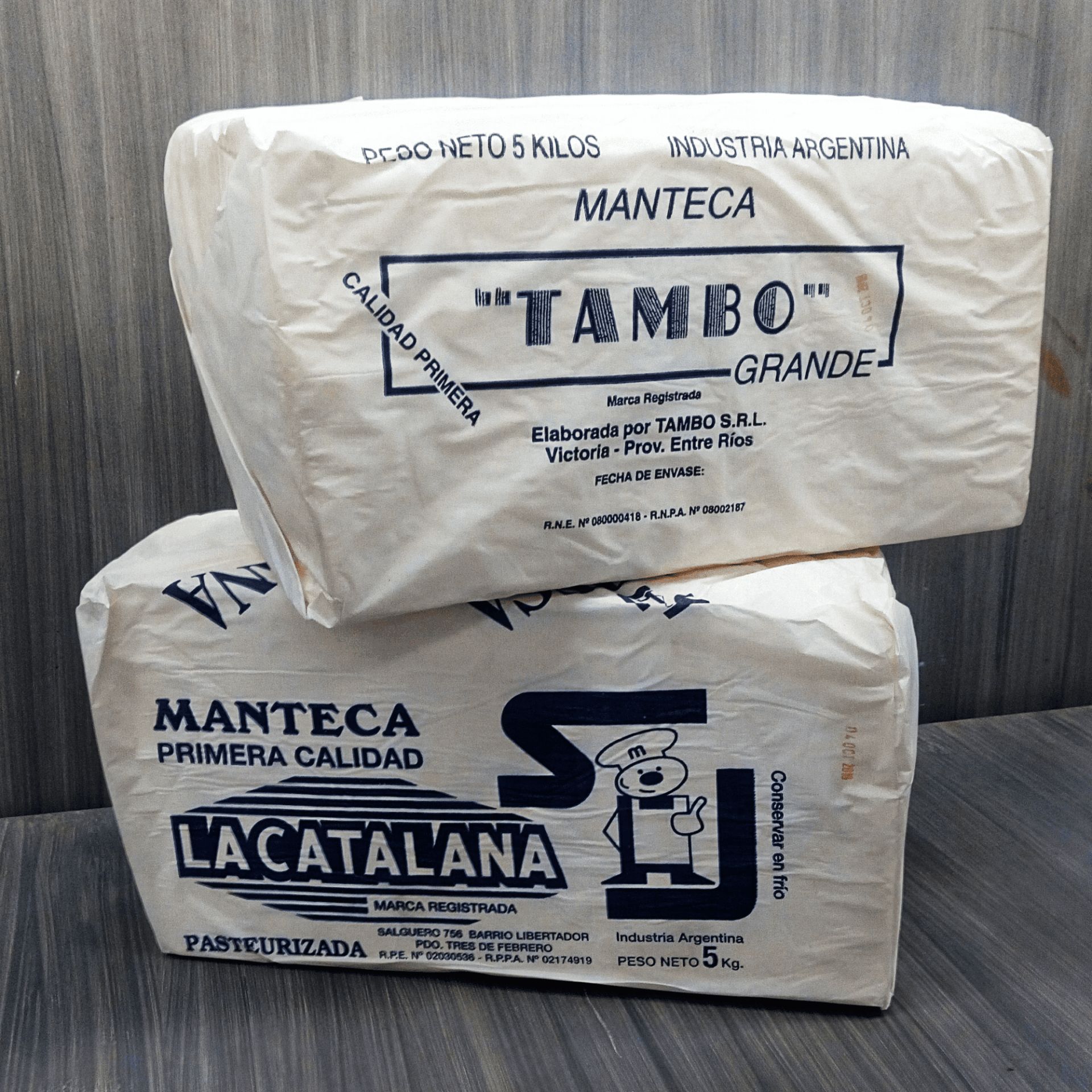 Bloques de productos lácteos envueltos apilados con las etiquetas TAMBO y LA CATALANA sobre una superficie lisa.
