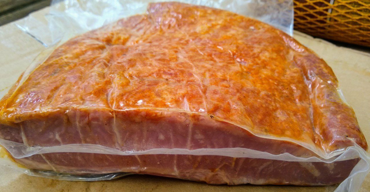 Trozo de carne curada envasado al vacío con condimento naranja en la parte superior y capas rosadas en la inferior.