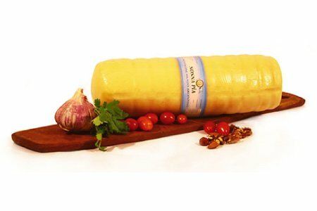 Rueda de queso amarillo sobre tabla de madera con ajo, hierbas y tomates cherry.