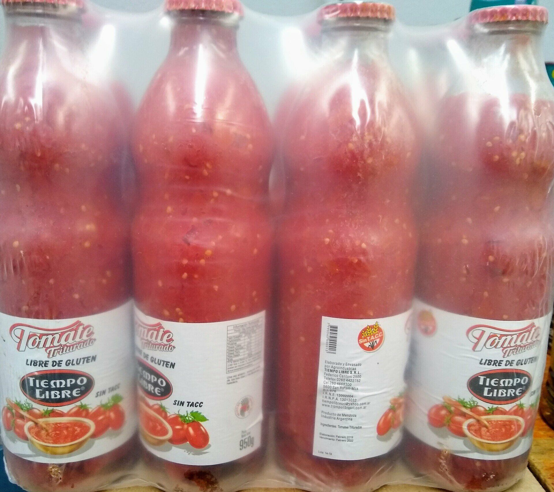 Cuatro botellas de jugo de tomate rojo en un estante, con etiquetas blancas y tapas rojas.