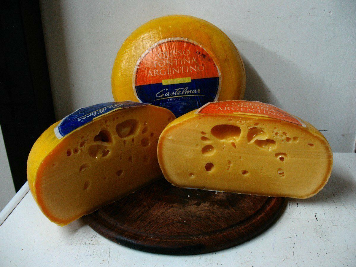 Tres ruedas de queso naranja sobre una tabla de madera, una de ellas cortada para que se vean los agujeros.