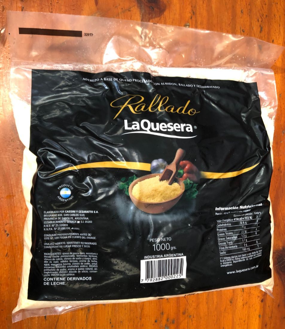 Paquete de queso La Quesera Rallado negro sobre una superficie de madera con un tazón de queso rallado.