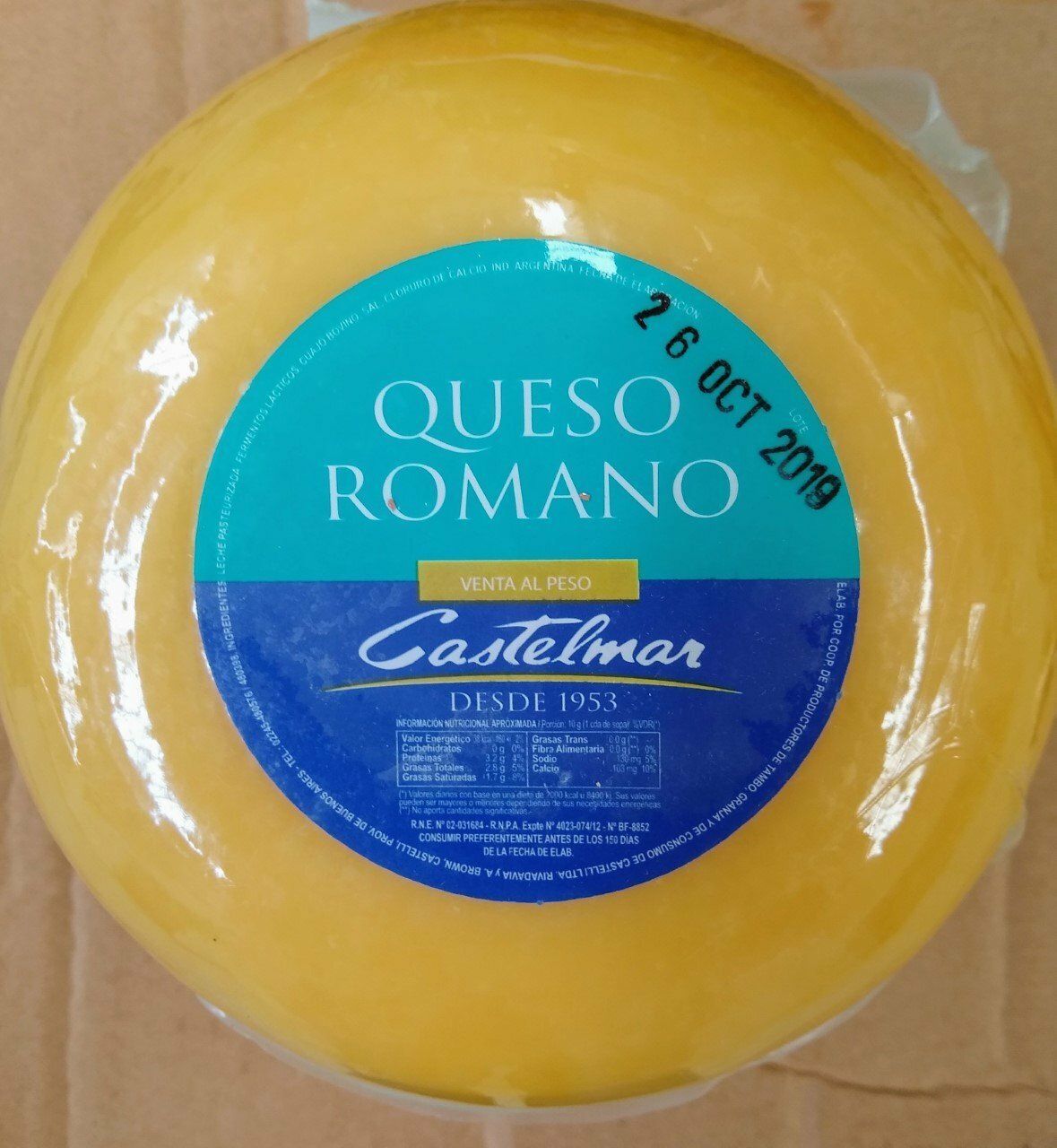 Rueda de queso romano redonda y amarilla con etiqueta azul de Castelmar sobre una superficie de cartón.