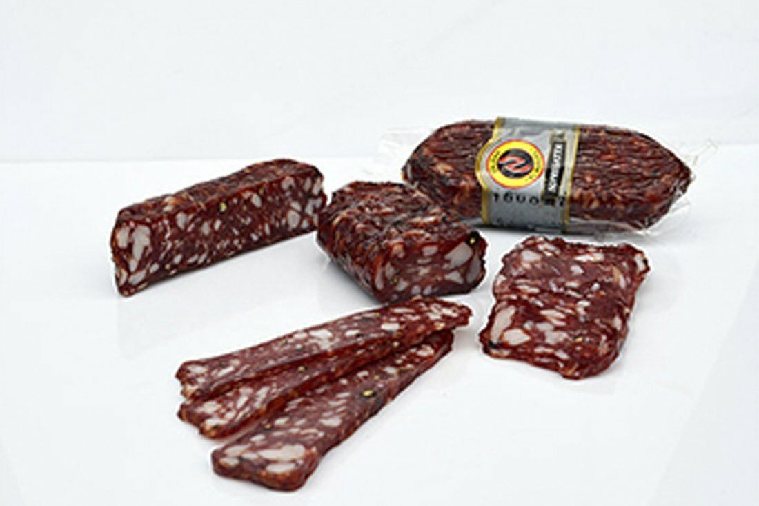 Surtido de salami y salchichas en rodajas sobre una superficie blanca, con un rollo envuelto al fondo.