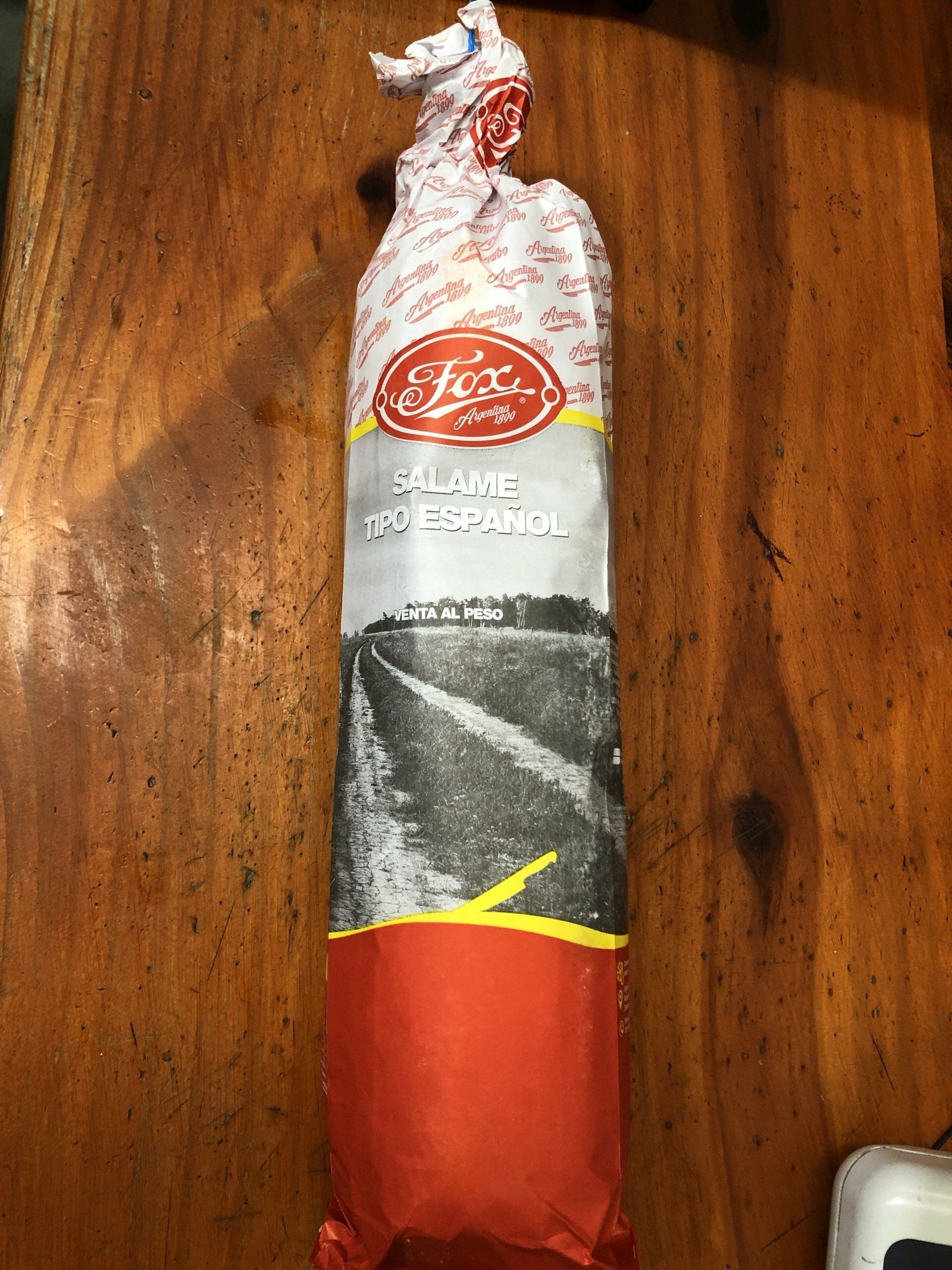 Paquete cilíndrico envuelto en rojo y plateado con la marca Fox, de pie sobre una superficie de madera.