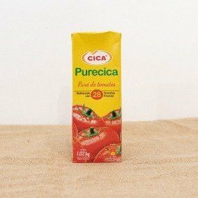 Envase de zumo de tomate Cica Purecica, de color amarillo y rojo, sobre una mesa beige.