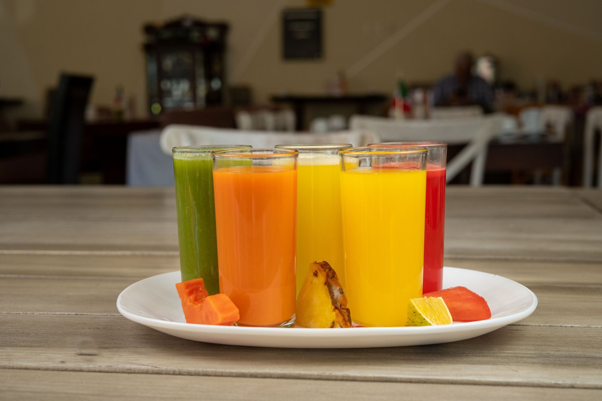 Batidos de frutas coloridos en vasos transparentes sobre un plato blanco encima de una mesa de madera.