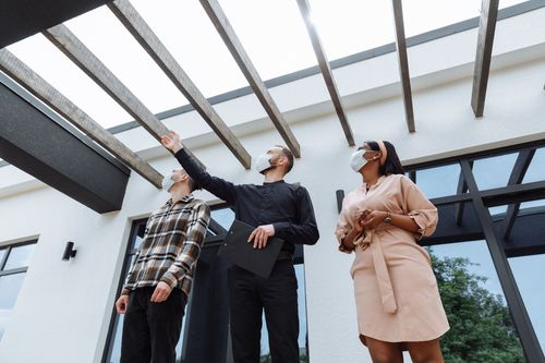 Three people in smart casual clothes looking up at a glass pergola outdoors