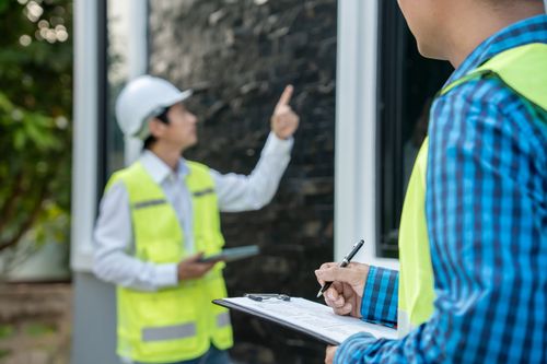 Two workers in safety vests inspecting a site, one taking notes on a clipboard.