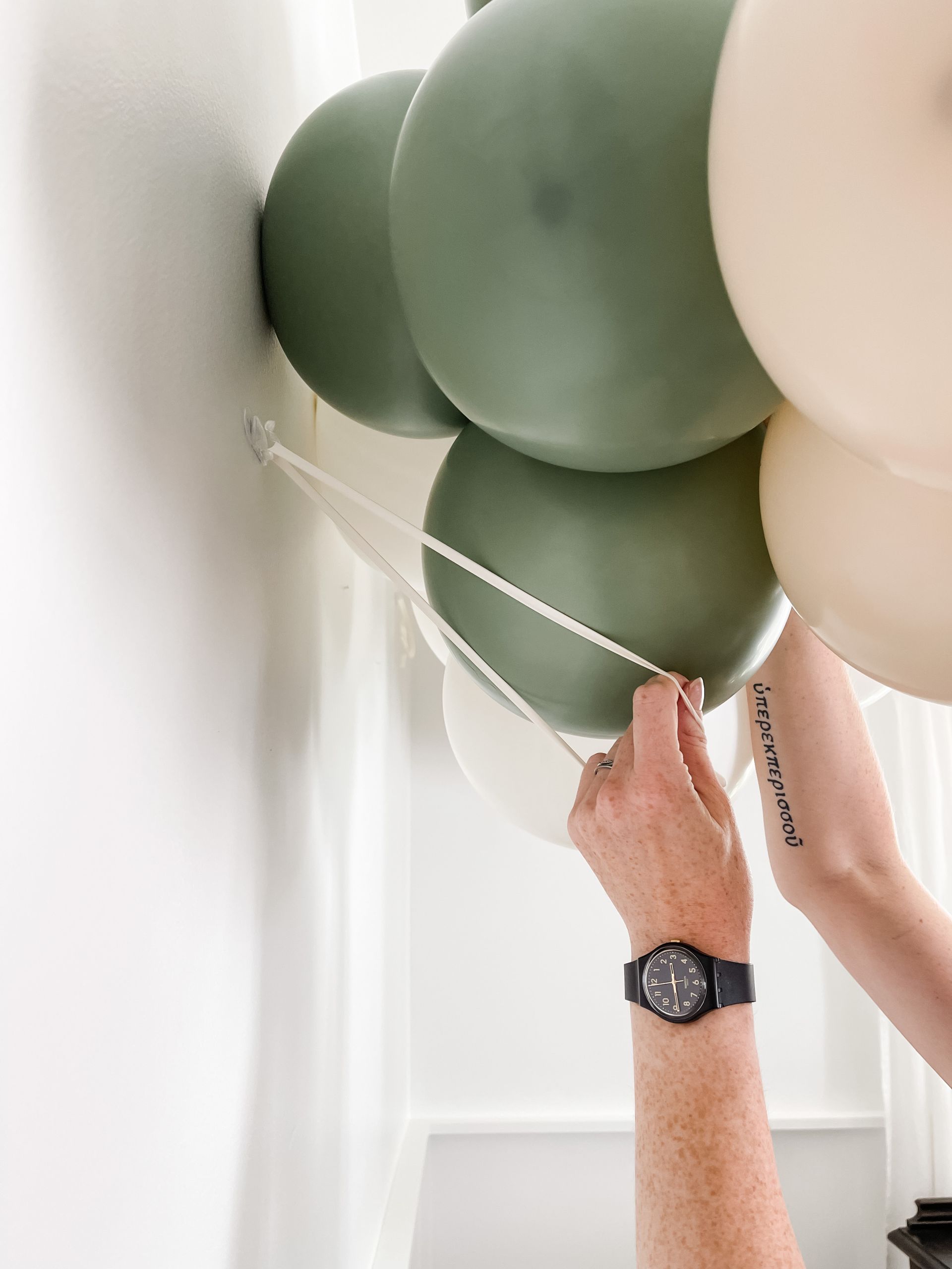 A person wearing a watch is tying balloons to a string.