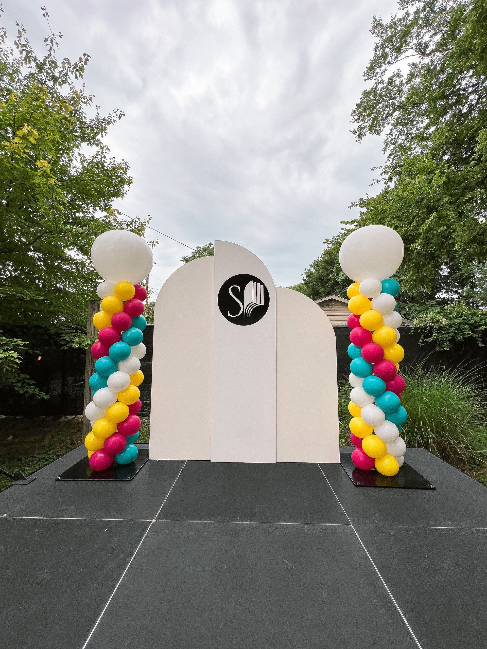 a white wall with a logo on it is surrounded by colorful balloons