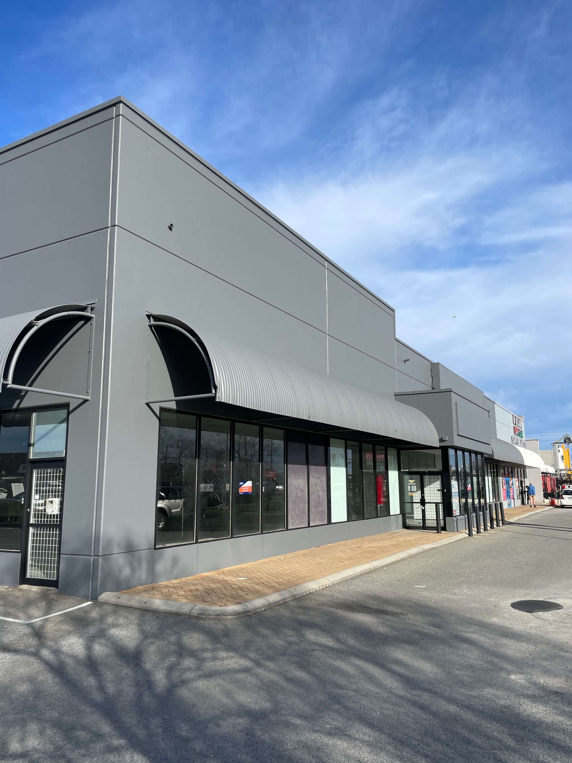 Gray commercial building with awnings, storefront windows, and a blue sky.