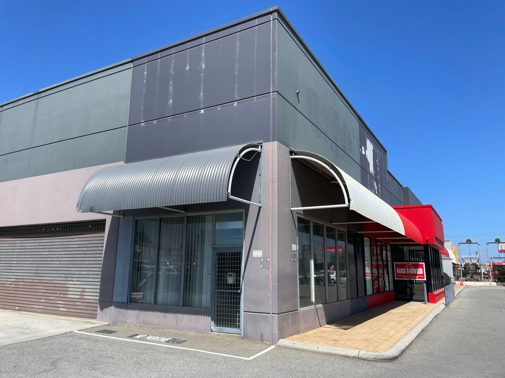 Exterior of a gray commercial building with awnings over windows under a clear blue sky.