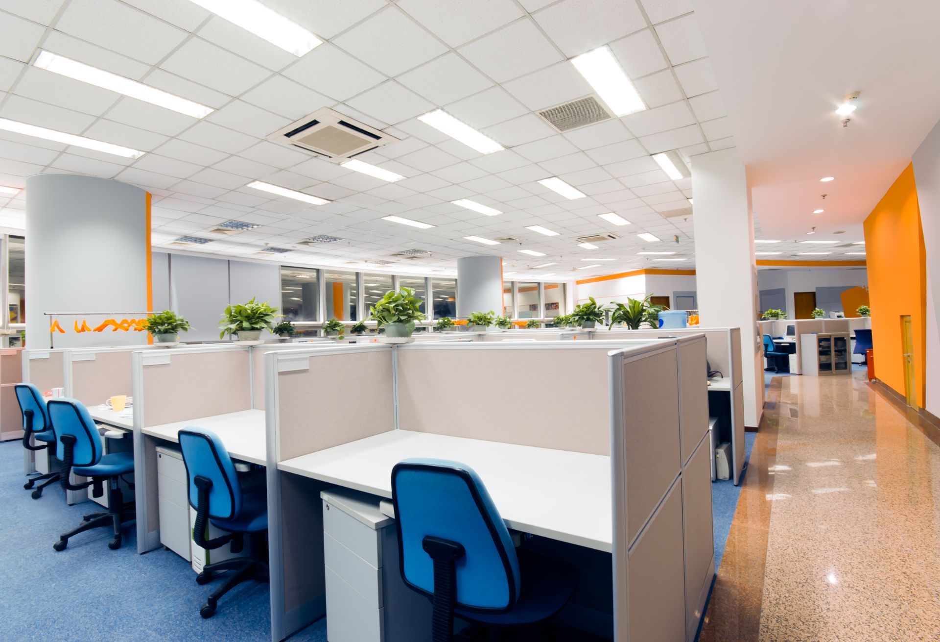 Organised office workplace with ergonomic furniture and a productive atmosphere. Open office with white cubicles, blue chairs, and orange accents.
