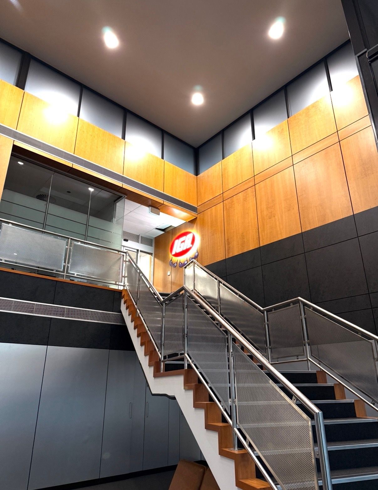 Modern indoor stairwell with metal railings, wood-paneled walls, and recessed ceiling lights.