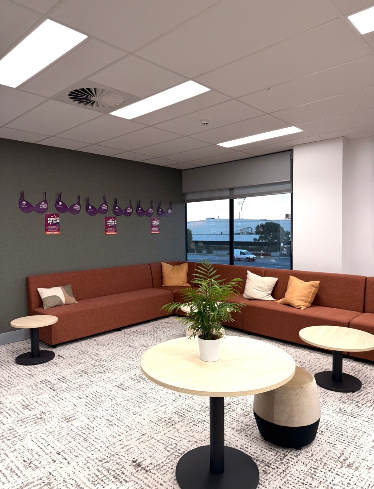 Modern lounge with brown sectional sofas, round tables, wall hooks, and a large window view