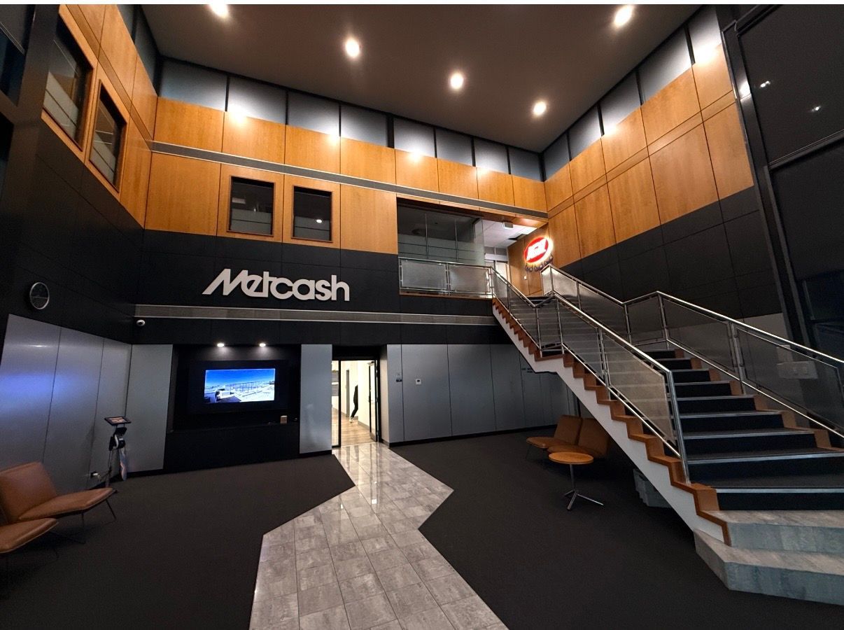 Modern lobby with wooden walls, black ceiling, stairs, and a mezzanine level above a Netcash sign