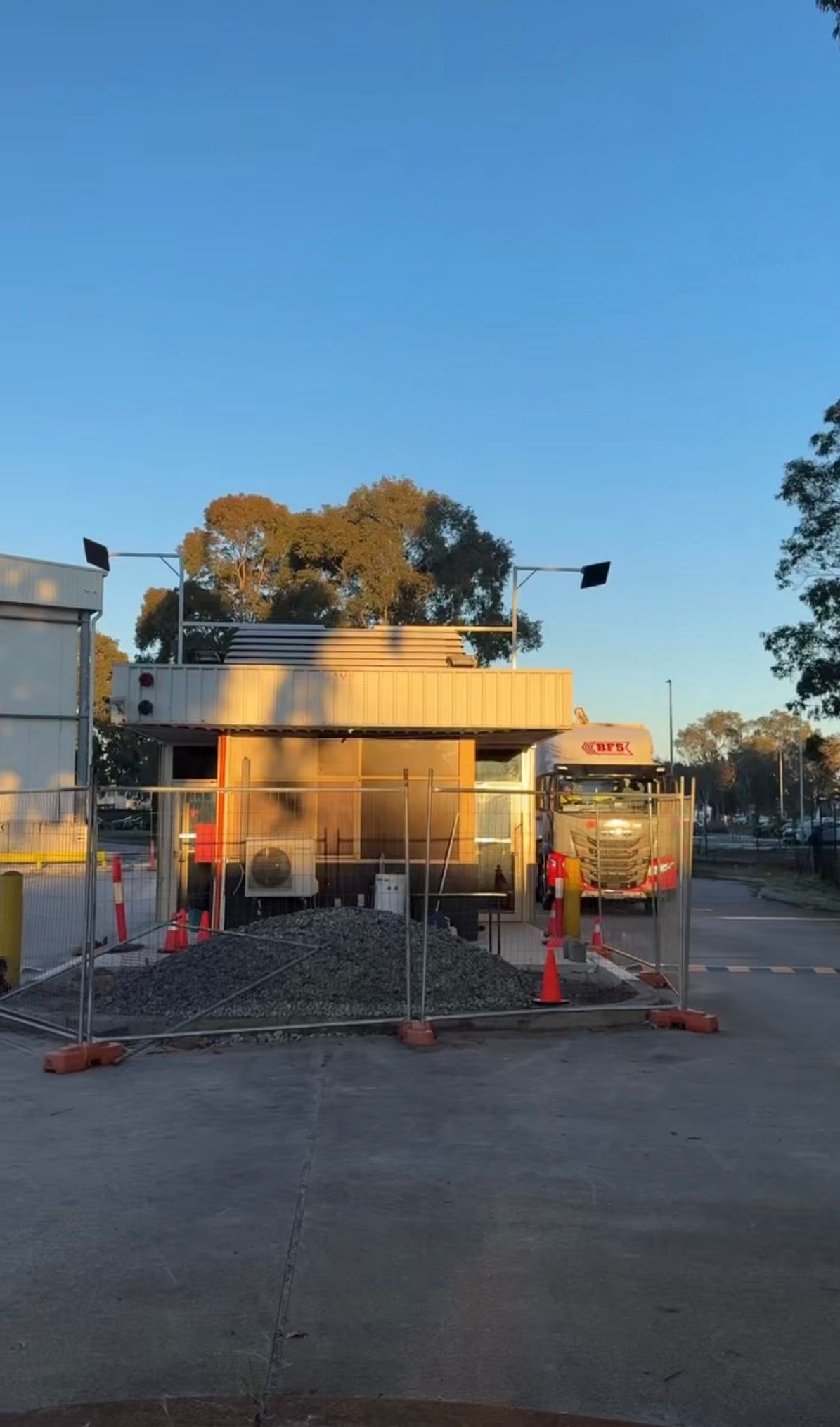 Construction site with a house under renovation, scaffolding, fencing, and a pile of gravel at dusk