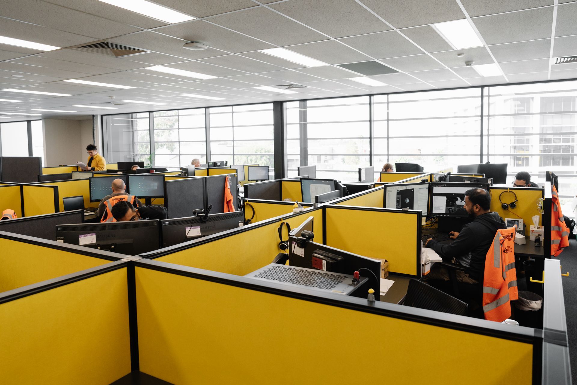 Office workspace with yellow cubicles, computers, and employees working.