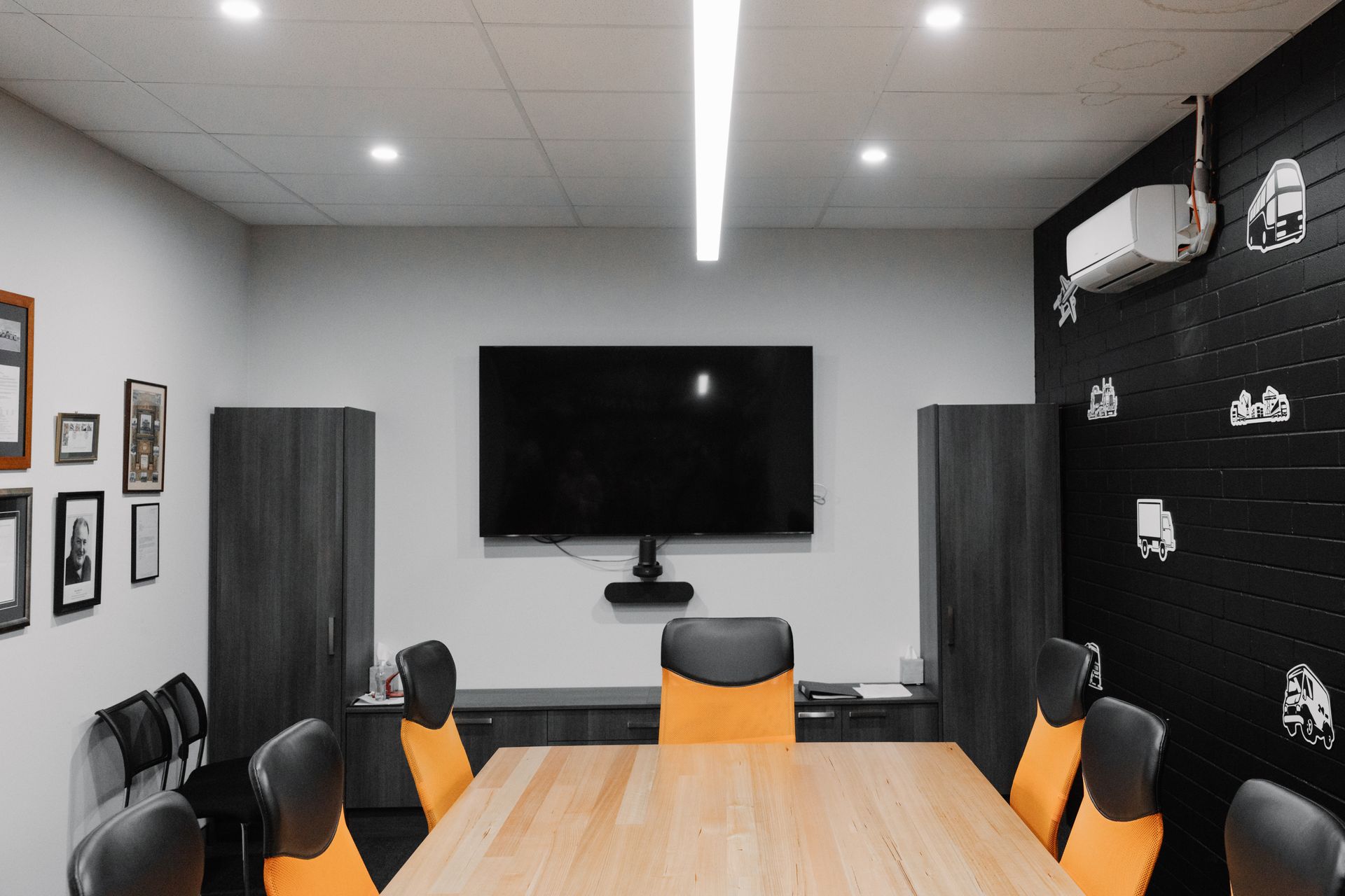 Conference room with a large screen, wooden table, and orange chairs. Dark accents and bright lighting.