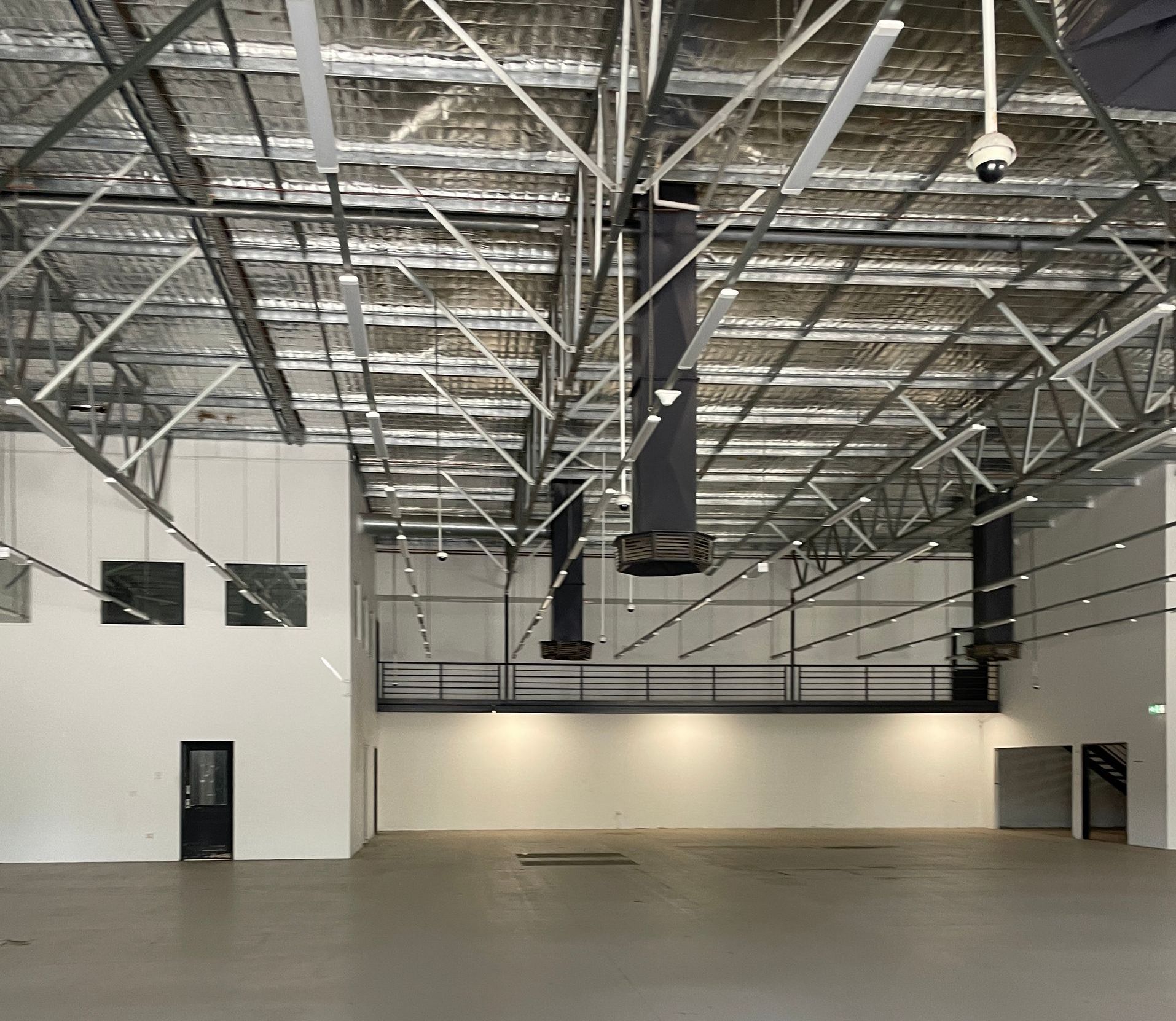 Large, empty warehouse interior with high ceilings, exposed beams, and concrete floor.