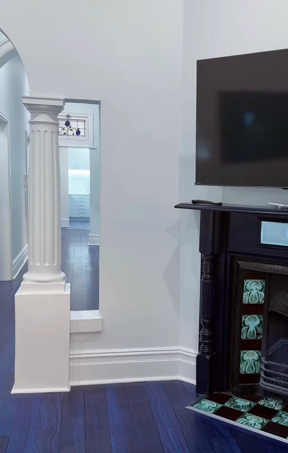 Living room corner with white column, wall-mounted TV, dark fireplace, and blue carpet