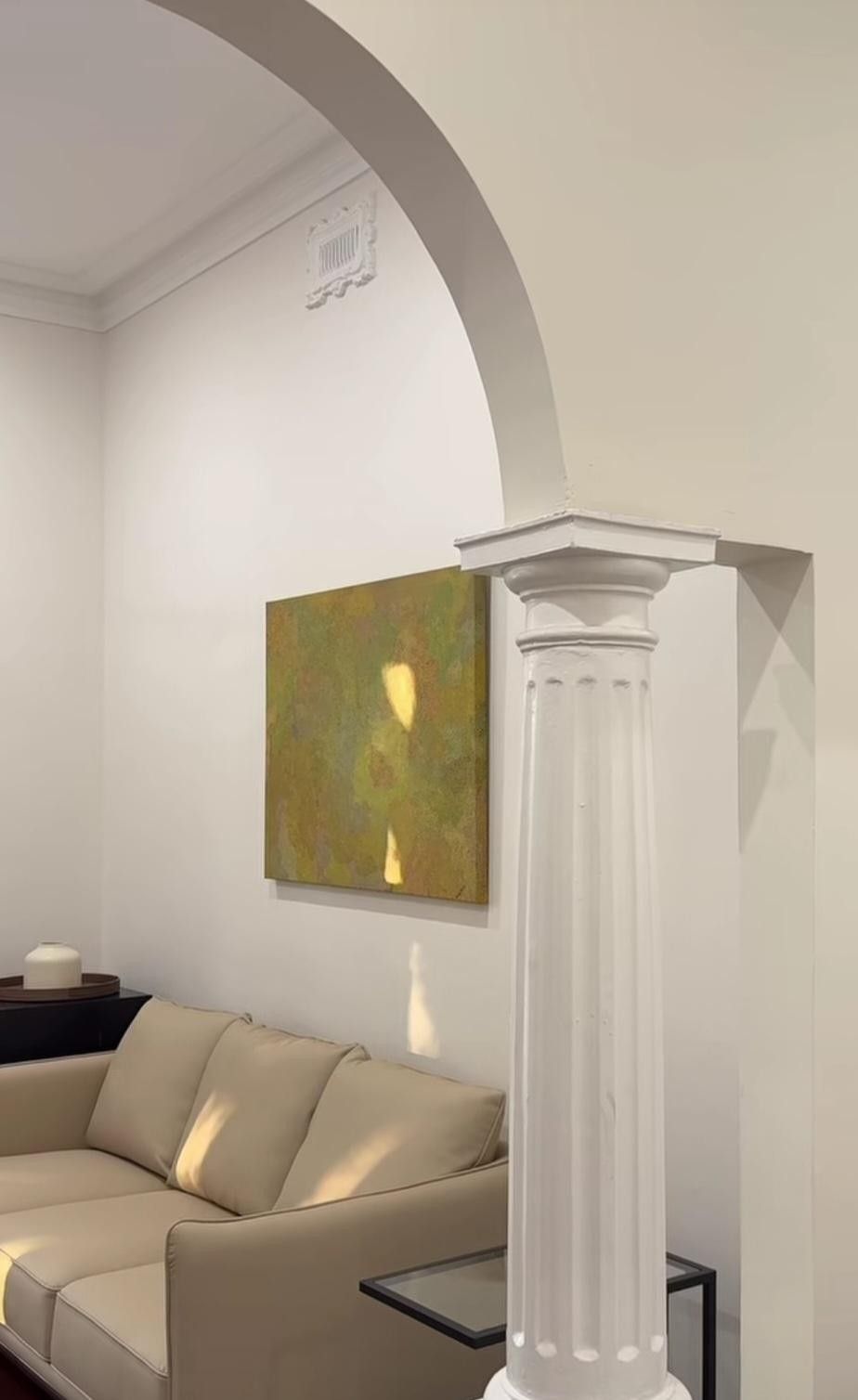 Elegant living room with white arch and column, beige sofa, and abstract painting on the wall
