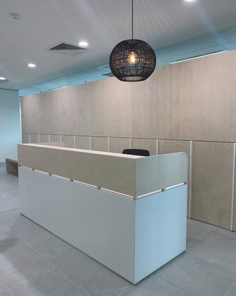 Reception desk in a modern office with light-colored walls and a decorative black pendant light.