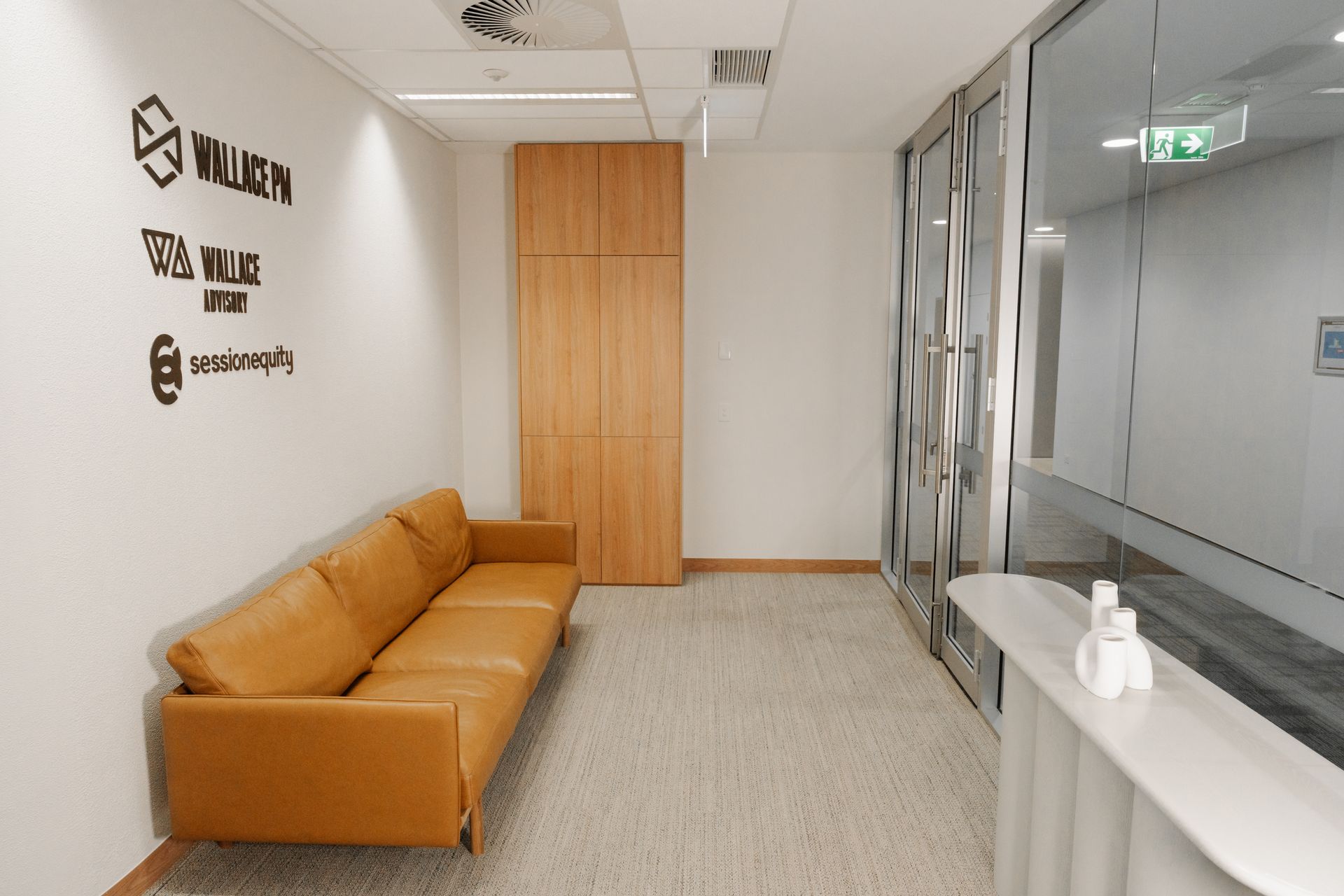 Office waiting area with tan sofa, wooden cabinet, white counter, and glass wall.