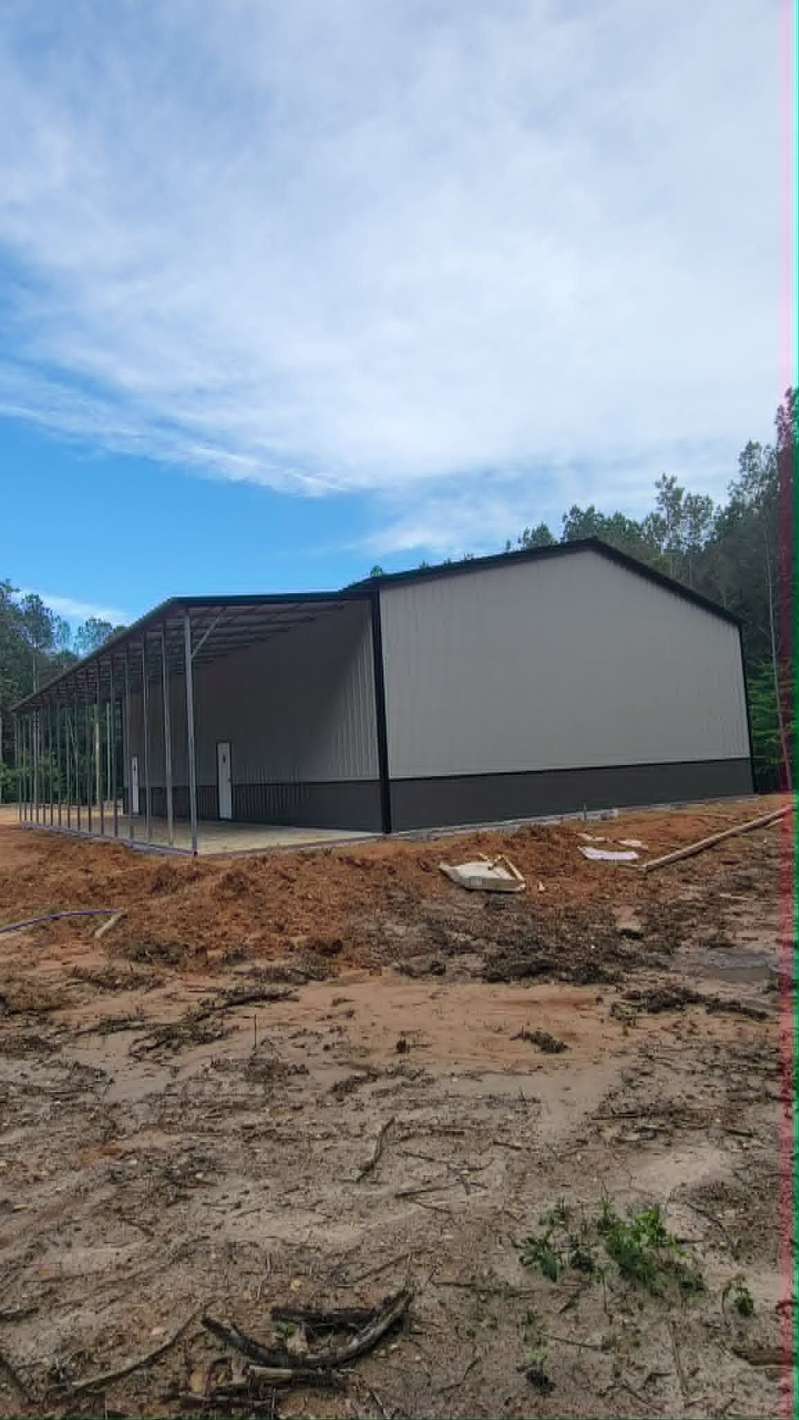 Large gray building under a blue sky, surrounded by trees and bare ground