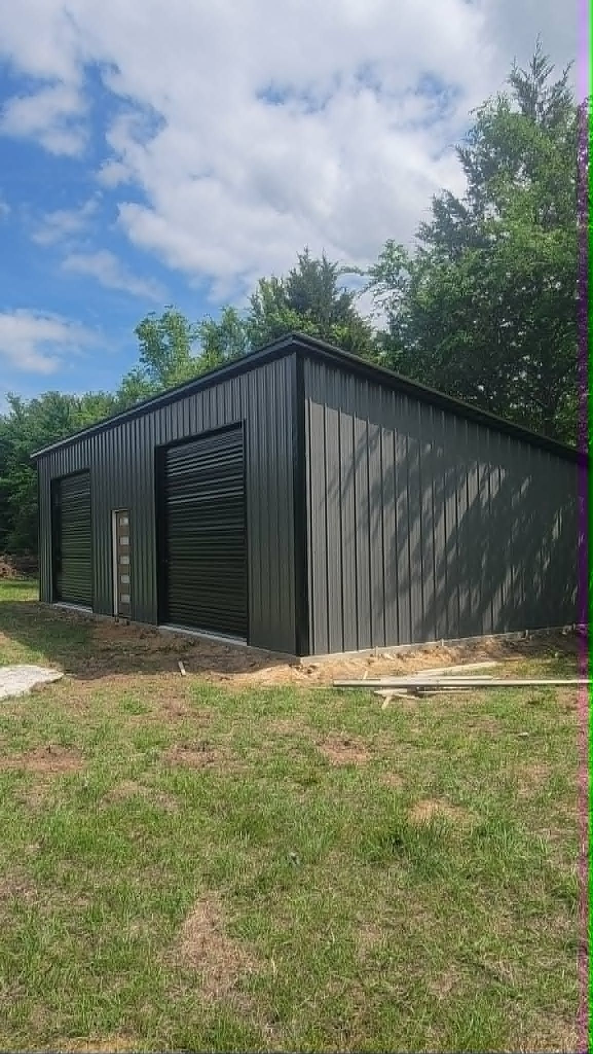 Black metal shed with a slanted roof on a grassy hillside under a cloudy sky.