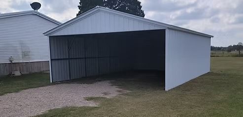Open-sided metal carport with white roof and siding on a grassy yard beside a house