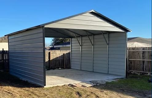 Metal carport with a concrete floor and open front in a fenced backyard under a blue sky