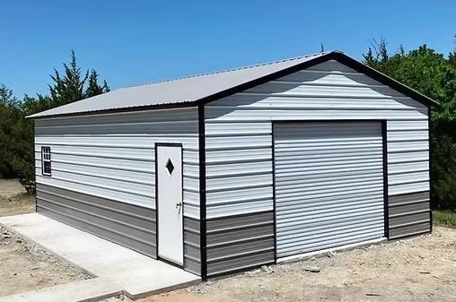 Gray metal storage shed with white trim, side door, and roll-up garage door under a clear blue sky