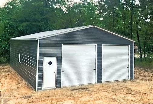 Gray metal garage with three white doors on a sandy lot, trees in the background