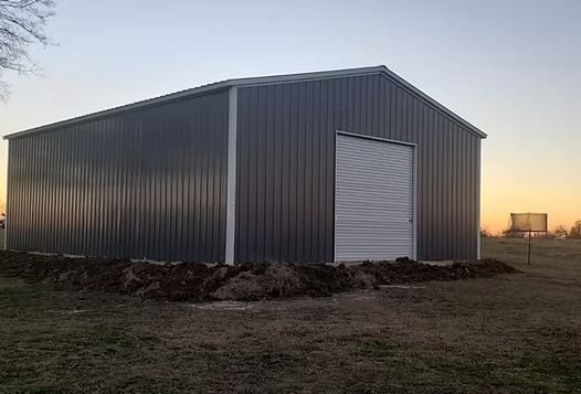 Gray metal storage building with a white roll-up door at sunset, on a grassy field