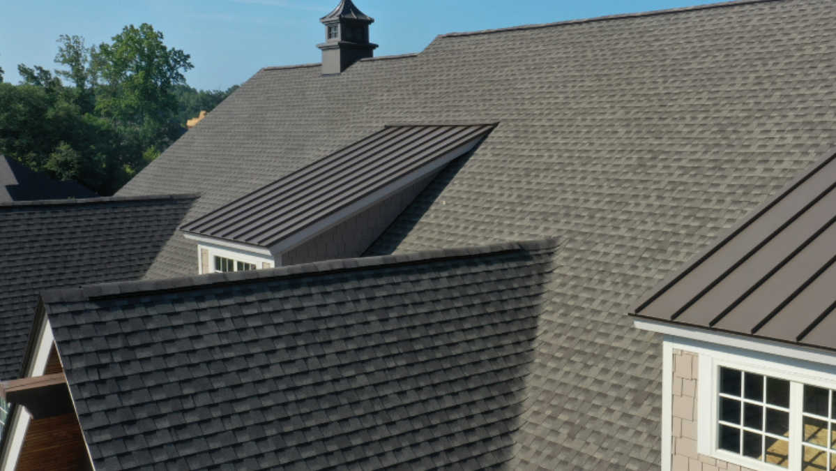 Roof with dark gray shingles and a small solar panel on a house under a blue sky