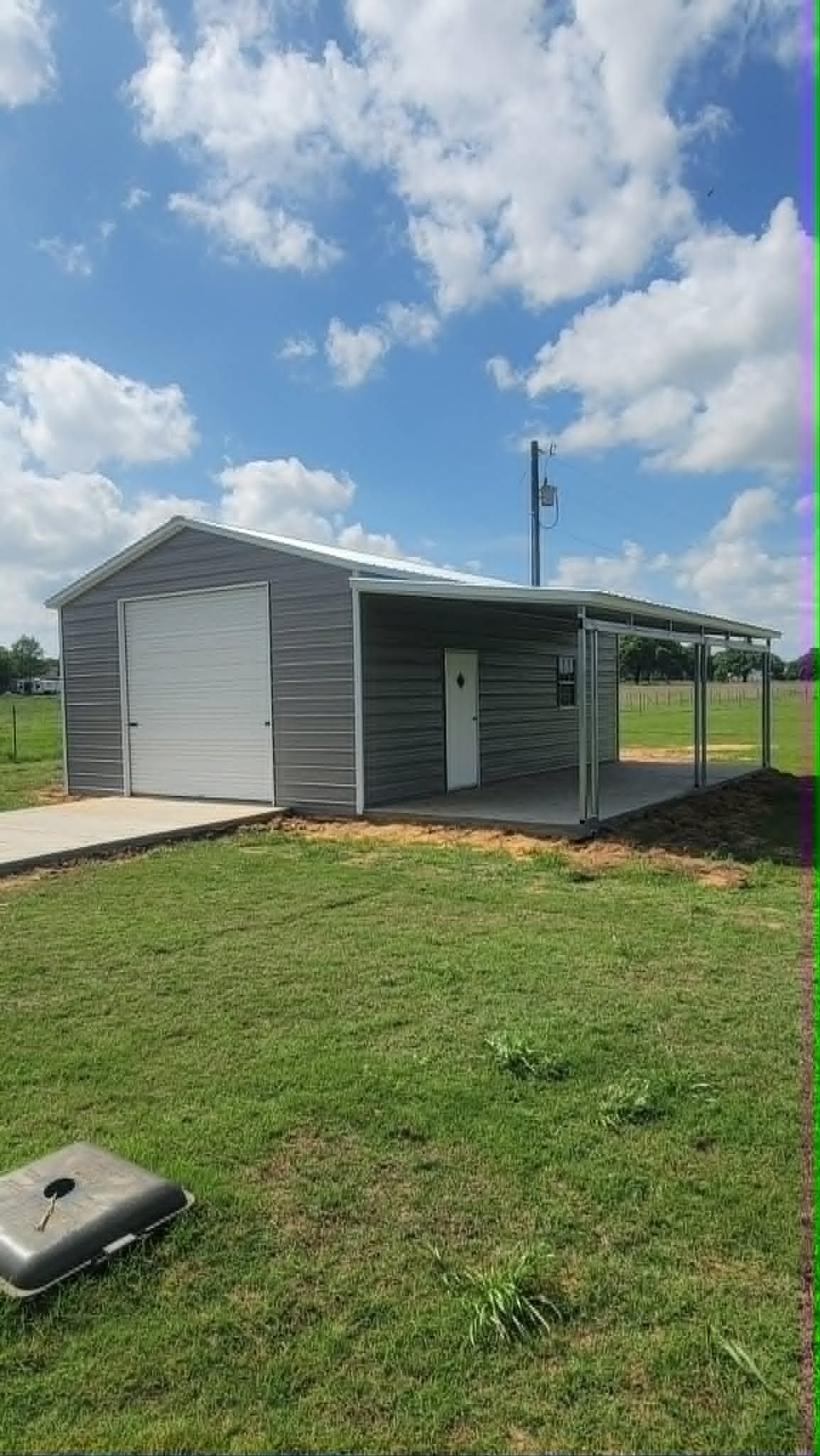 Small corrugated-metal shed with a white front wall on a grassy field under a partly cloudy sky