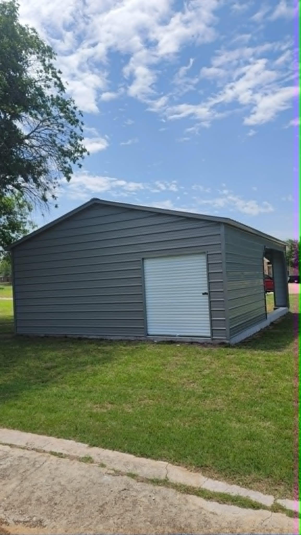 Gray metal shed with a white door on a grassy lawn under a partly cloudy sky