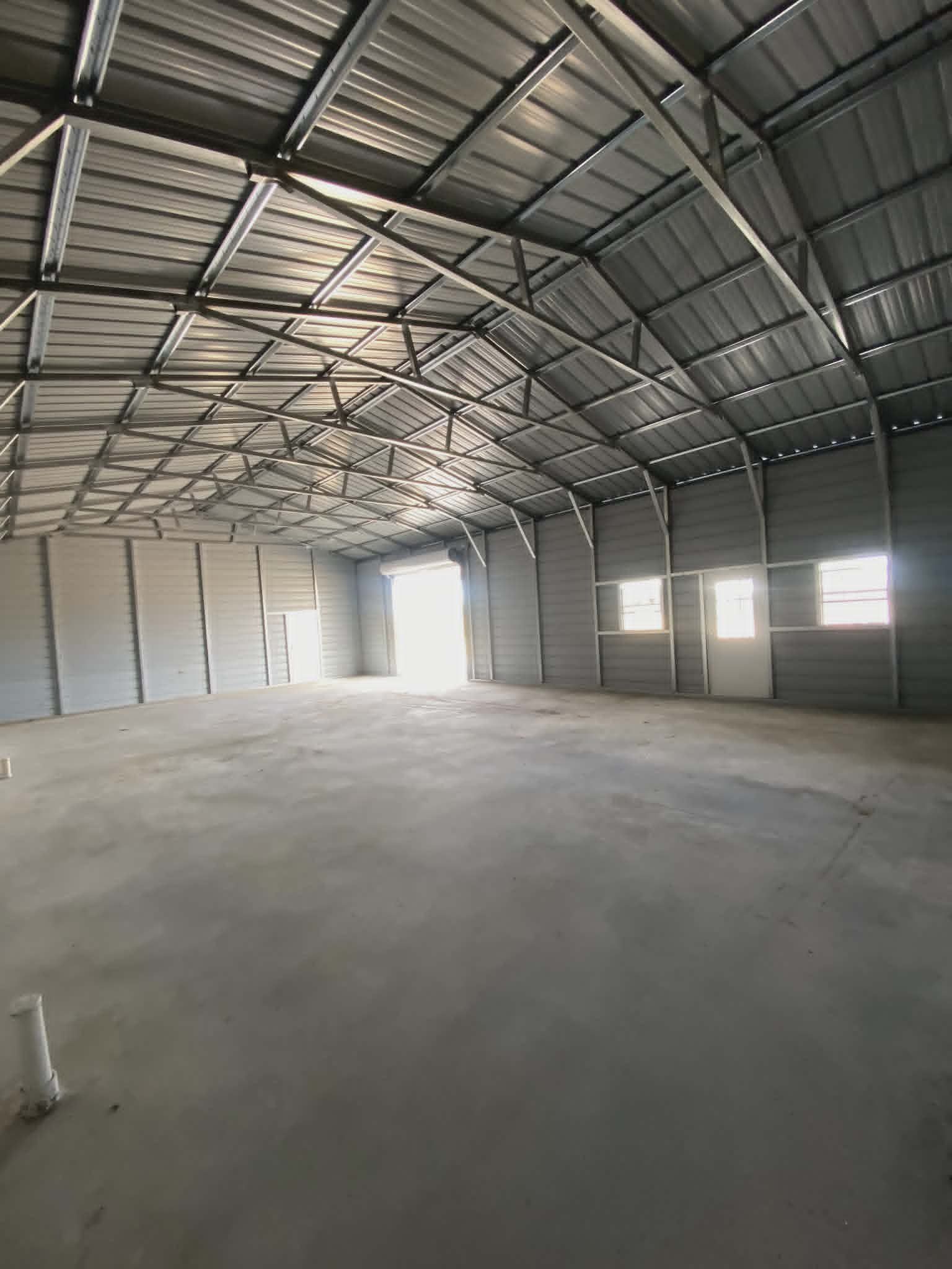 Empty metal warehouse interior with concrete floor and bright light from open doorway