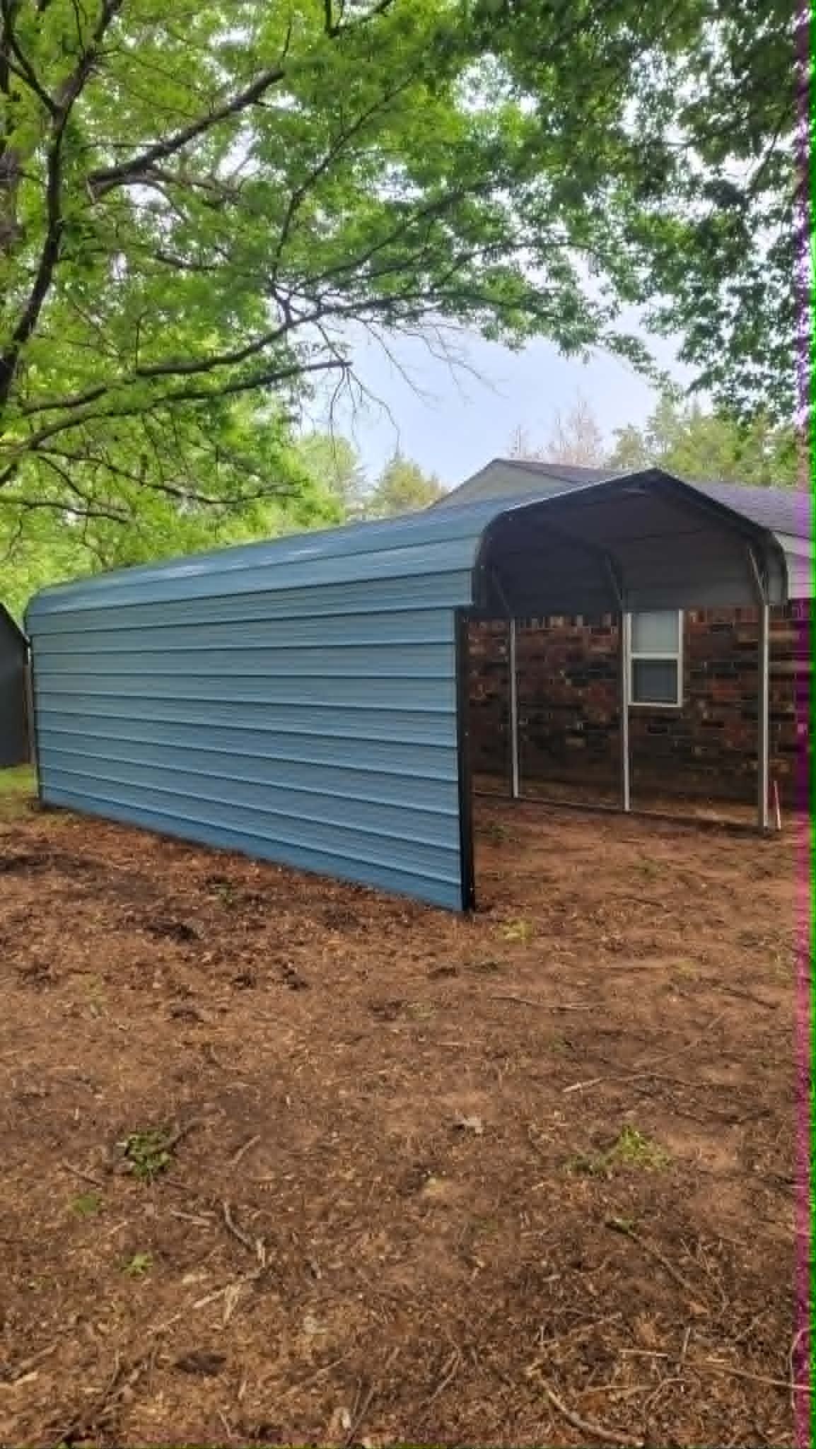Blue tarp-covered shelter in a wooded area with open front and metal frame