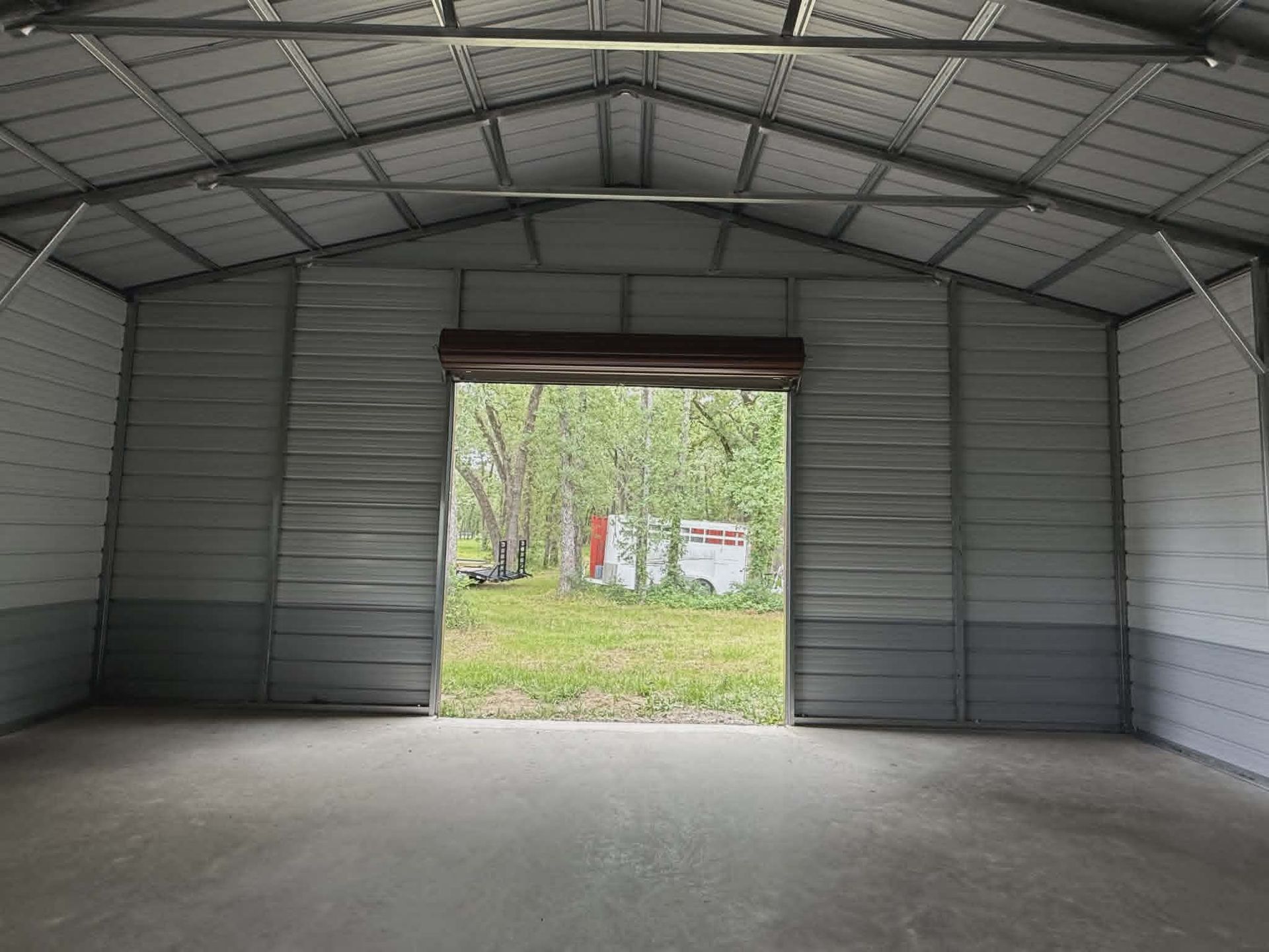 Empty metal shed interior with open doorway facing a grassy yard and trees