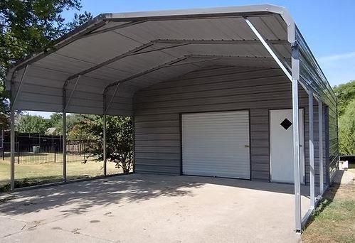 Covered carport with a metal roof and roller door beside a white shed on a concrete pad