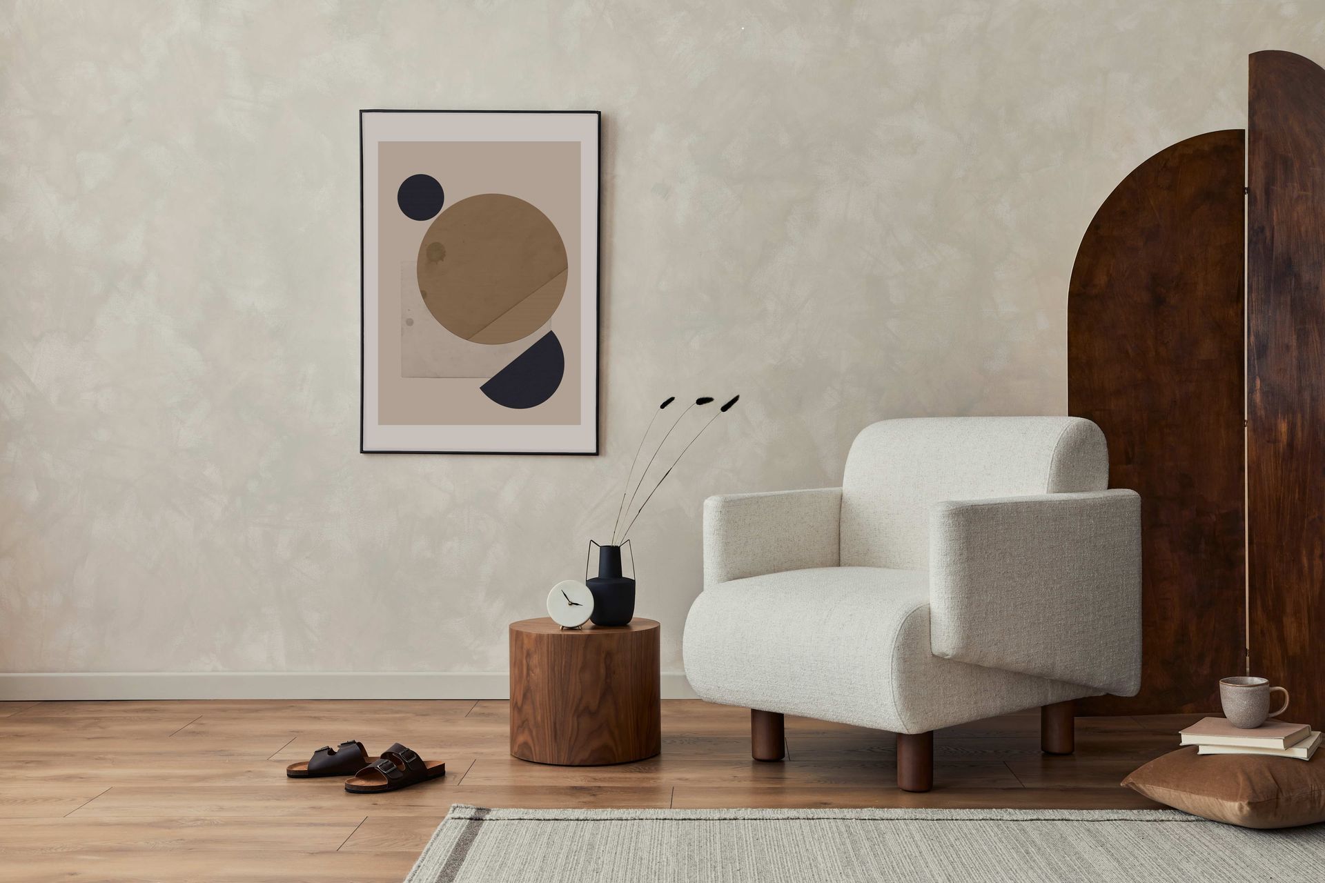 Minimalist living room with white armchair, framed wall art, wooden side tables, and shoes on a wood floor.