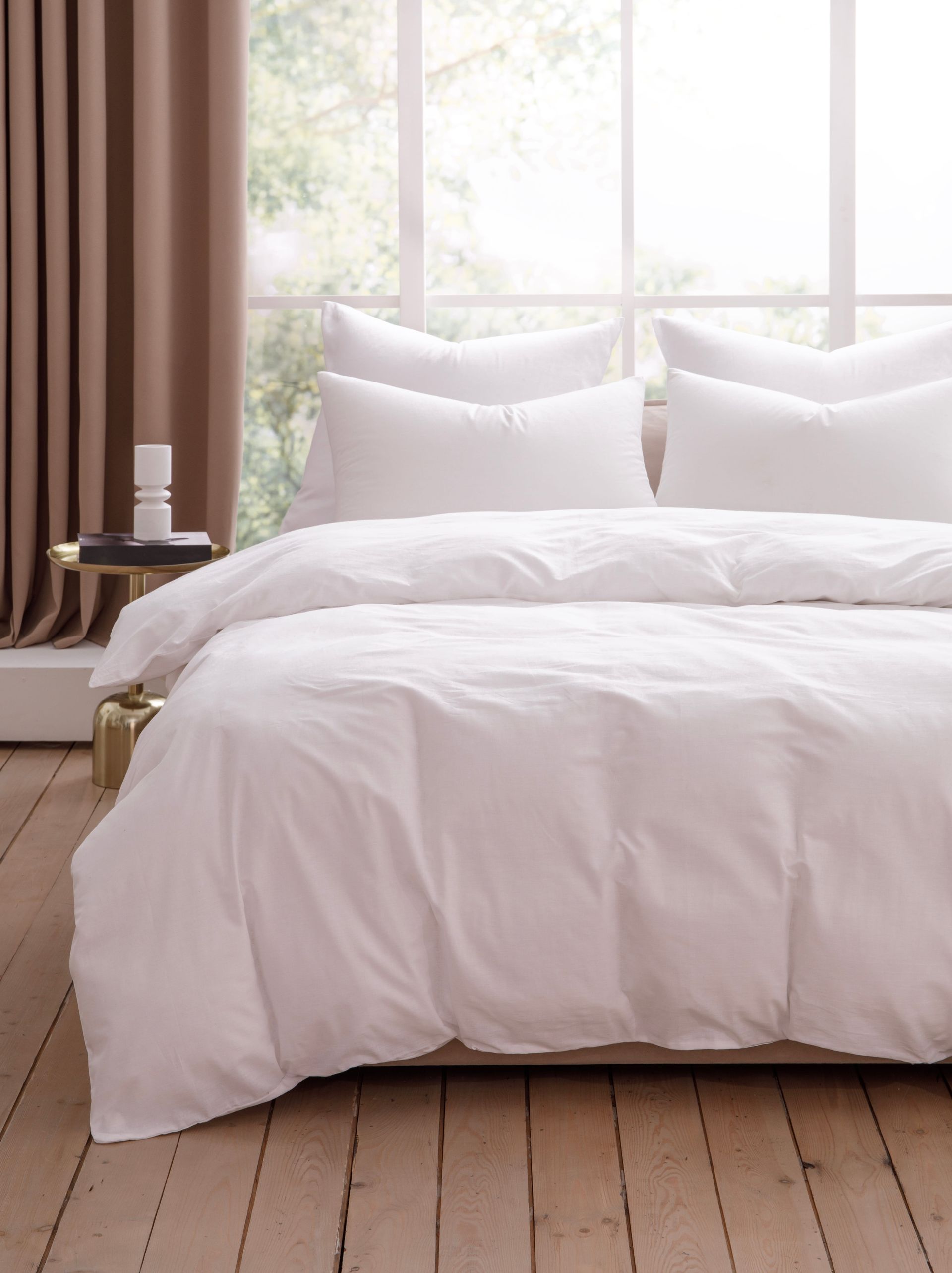 Bright bedroom with white bedding, pillows, wood floor, and a window with curtains.