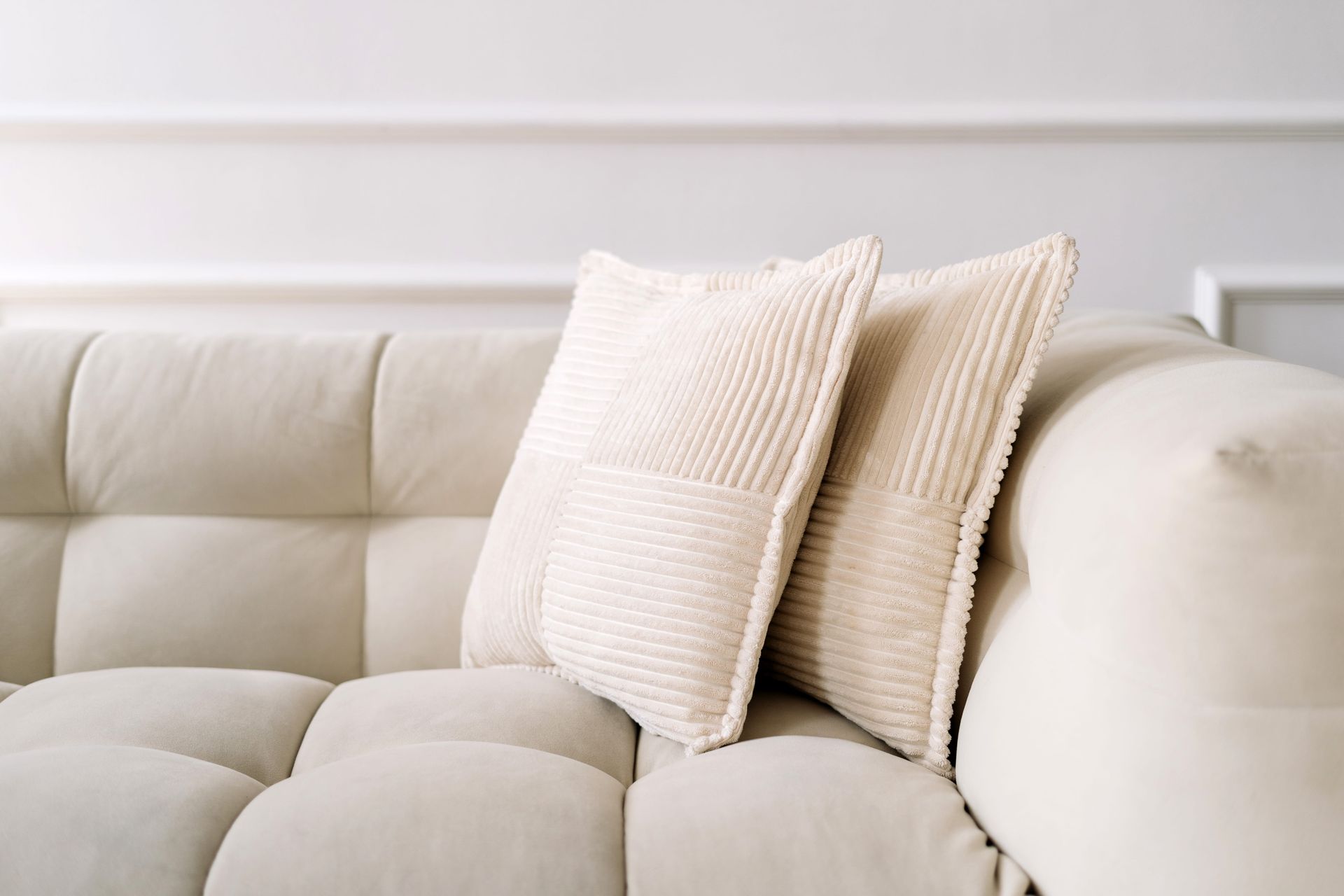 Cream sofa with two textured beige pillows against a light wall.