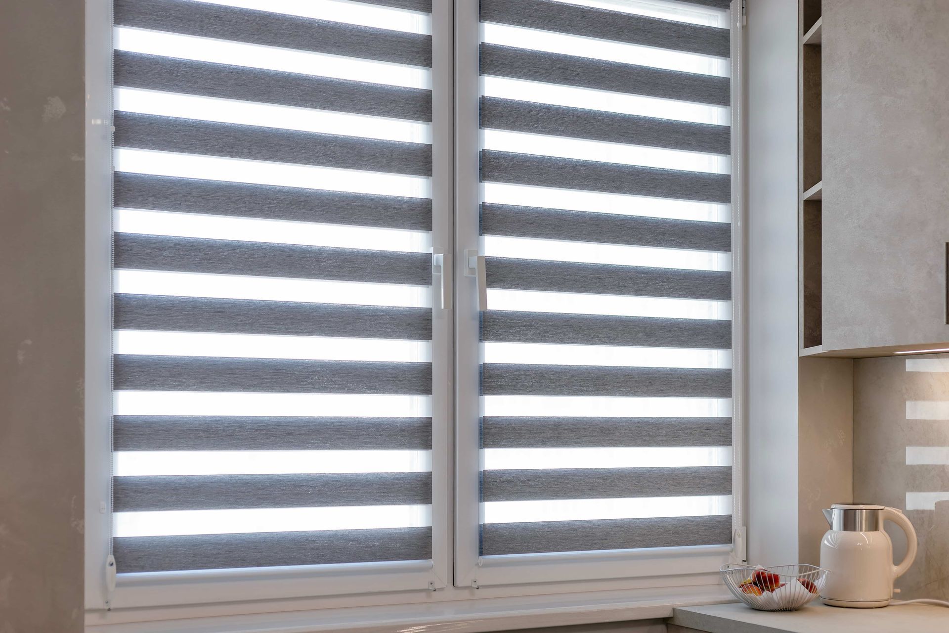 White kitchen window with striped zebra blinds, a mug, and a small plant on the sill