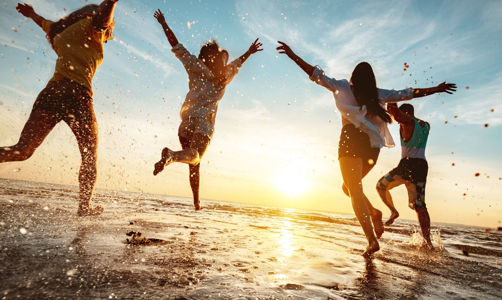 Vier Personen springen und planschen bei Sonnenuntergang im Meerwasser.mit